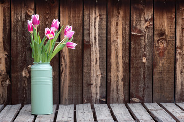 Bunch of bright pink tulips in a green container on a rustic plank table.