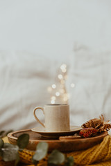 Coffee cup placed on a wooden tray and warm sweater with background bokeh blur of lights. Morning in Bed. Still Life Composition with Copy Space