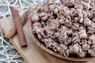 chocolate flavored popcorn in the yellow glass and on the brown wood table with cinnamon background