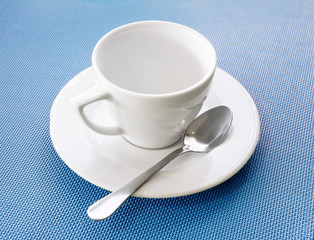 White porcelain empty tea or coffee cup on a wood table with a spoon and saucer.