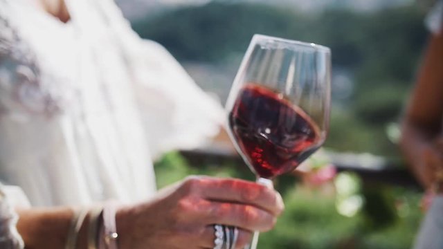 Hand of adult unrecognizable woman shakes glass of red wine outdoors on hot summer sunny day