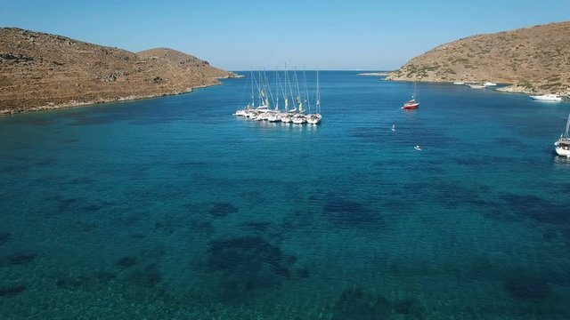Yacht regatta anchored in the Gulf of the Mediterranean Sea near the Kolona beach. Eight luxury yachts linked while yachtsmen resting under the sun. Apokrisi, Kithnos island, Cyclades, Greece.  Aerial