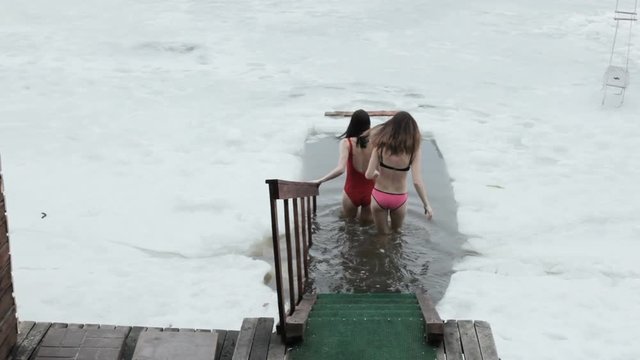 Young women in swimsuit splashing in an ice hole.