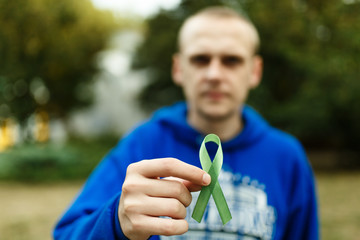 green ribbon symbol of  fight against cancer of lymphoma, in the hands of a man