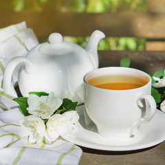Hot green tea in a teapot and cup with a branch of jasmine flowers blossom  and white towel on rough rustic brown wooden background.  Nature healthy slow life concept.