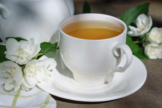 Hot green tea in a teapot and cup with a branch of jasmine flowers blossom  and white towel on rough rustic brown wooden background.  Nature healthy slow life concept.