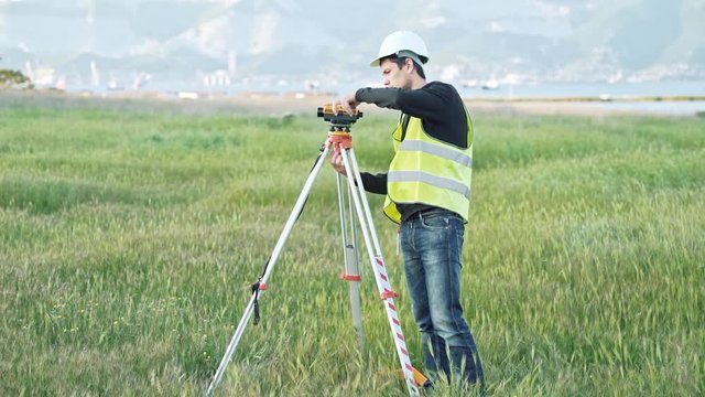A male surveyor in work clothes adjusts the equipment on the construction site. The concept of landscape design, geodesy