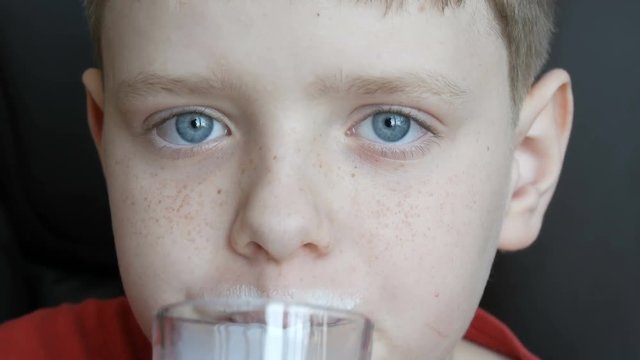 Teenager boy with blue eyes and freckles drinking milk from a glass beaker and wiped his milk mustache