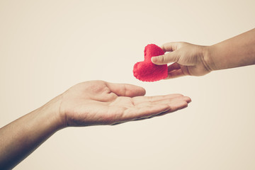 Baby's hand giving a red heart to mother's hand / Love and care between kid and mom / Mother's day concept