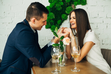 Cheerful young man and woman are dating in restaurant. They are sitting at the table and looking at each other with love.