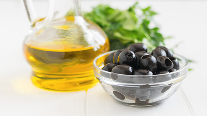 Olives, herbs and a bottle of olive oil on a white table.