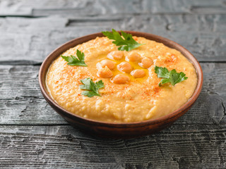 Clay bowl with fresh hummus on a wooden table.