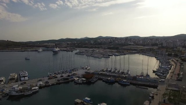 Flying over marina, port, yacht parking of Lavrio coastal city. Yachts, sail boats, cruise ships along the waterfront of the Aegean Sea bay at sunset. Attica, Greece. Aerial footage.