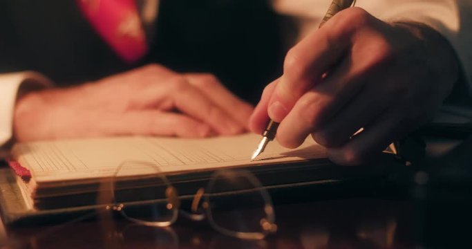 1940s period piece of businessman hands using a classic fountain pen to make entries into a company ledger.