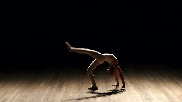 A small very flexible girl does a back flip on black background, slow motion. Silhouette.