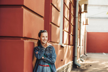 Cheerful little girl in jeans clothes stands near an old restored beautiful building.