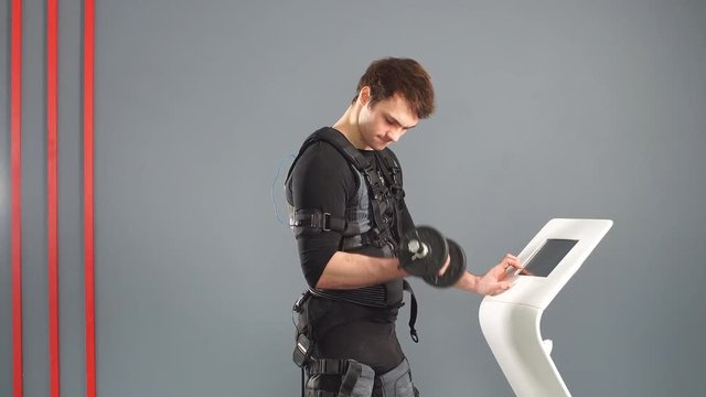 Fit man in Electrical Muscular Stimulation suit standing with dumbbells.