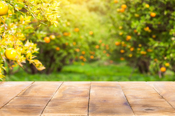 Wood table top on shiny sunlight with blur of orange garden in the morning.