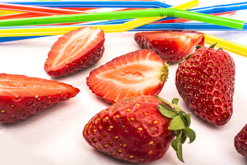 Strawberries and straws scattered on a white background