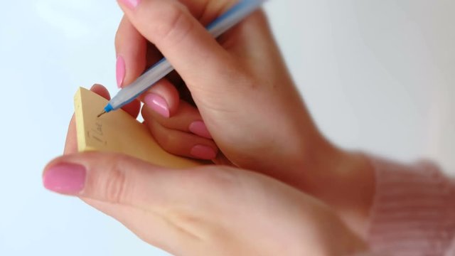 Close up woman's hands writing note "I love you" kisses the paper, leaving a trail of lips of lipstick and sticks it on the wall.