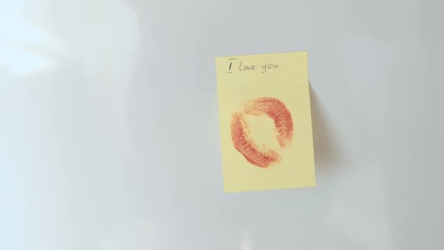 Closeup woman's hand stick the note with kiss and write "i love you" on white wall.