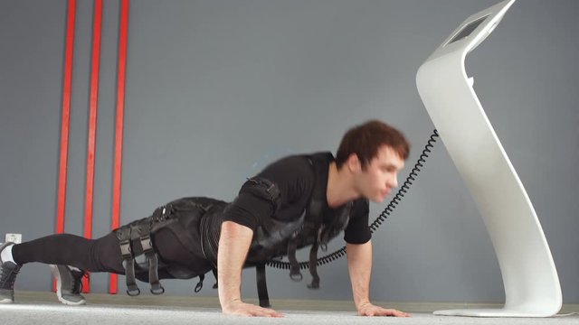 EMS male working out, doing push ups while connected to electric muscle stimulator.