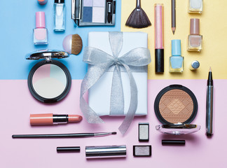Naklejka premium Beauty, decorative cosmetics and gift box with bow. Makeup brushes set and color eyeshadow palette on bright multicolor and blue background , flat lay, top view, Minimalistic style.