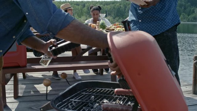 Man in sunglasses grilling sausages at picnic by lake