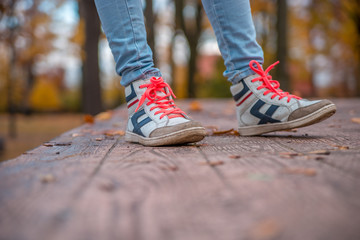 The girl's feet in sports shoes on the background of the autumn Park.