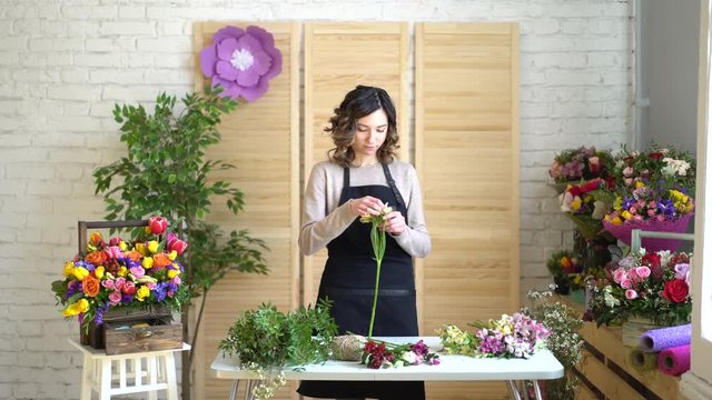 Florist at work: pretty young blond woman holds fashion modern bouquet of different flowers with peone and roses in craft paper