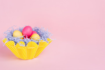 Easter painted eggs in fun yellow basket on soft pink background, copy space.