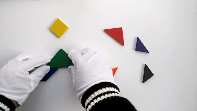 man playing wooden tangram and shaping it like a people sitting down on white