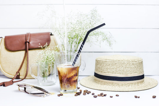 Milk is poured into a glass with a cold coffee with ice, which stands on a white table among the female summer accessories. Next to the dry bouquet gypsophila. Summer relax concept