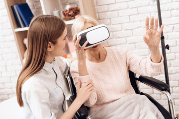 Girl is caring for elderly woman at home. Woman is using virtual reality.