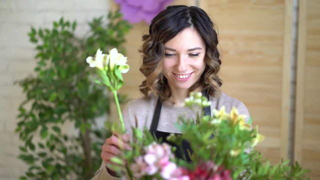 Florist at work: pretty young blond woman holds fashion modern bouquet of different flowers with peone and roses in craft paper