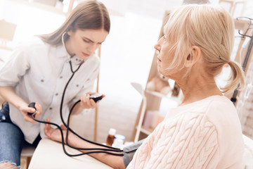 Fototapeta premium Girl is nursing elderly woman at home. Girl is measuring blood pressure with tonometer.