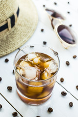 Cold coffee in a glass with ice. On the table among coffee beans and summer women's accessories. Summer relax concept