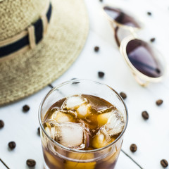 Cold coffee in a glass with ice. On the table among coffee beans and summer women's accessories. Summer relax concept