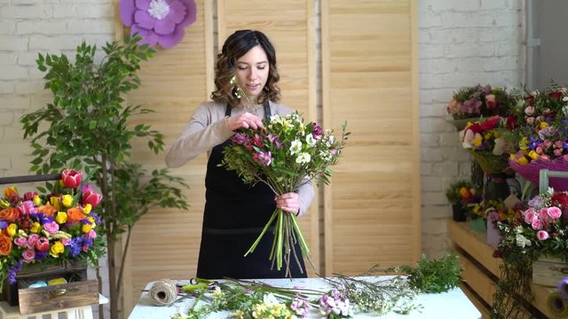 Florist at work: pretty young blond woman holds fashion modern bouquet of different flowers with peone and roses in craft paper