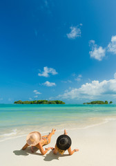 Fototapeta na wymiar Two women with hats enjoying sun holidays on the tropical beach