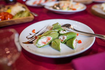 Green pancakes. Pancakes with spinach stuffed with cream cheese and fish on a white plate. 
