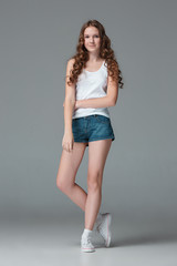 Full length of young slim female girl in denim shorts on gray background