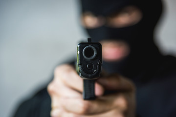 Masked robber with hand gun pointing aiming