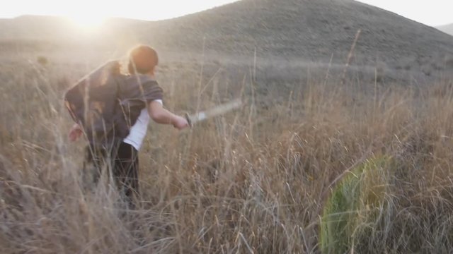 A boy with a sword runs to the horizon at sunset in grass. Slow Motion video