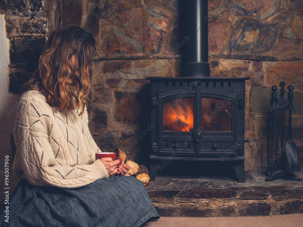 Wall mural Woman in white jumper by fireplace with mug