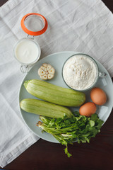 Ceramic plate with squash, garlic, parsley, two eggs, flour and sour cream near on wooden table. Ingredients for salad or garnish
