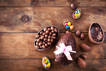 Chocolate Easter eggs on wooden background with ribbon bow and candies.