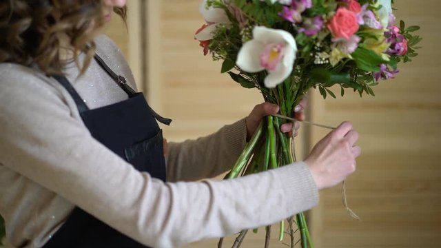 Florist at work: pretty young blond woman holds fashion modern bouquet of different flowers with peone and roses in craft paper