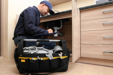 Plumber with set of tools repairing sink in kitchen