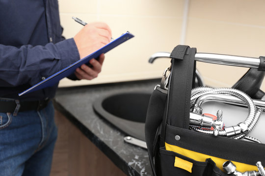 Plumber with set of tools and clipboard in kitchen